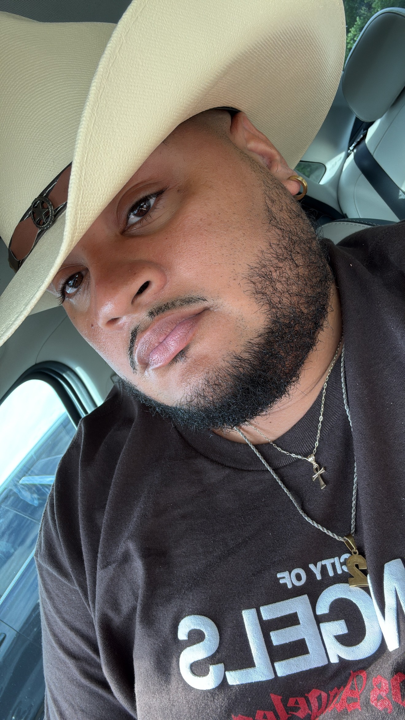 Man wearing a wide-brimmed hat and black shirt, sitting in a vehicle, looking at the camera.