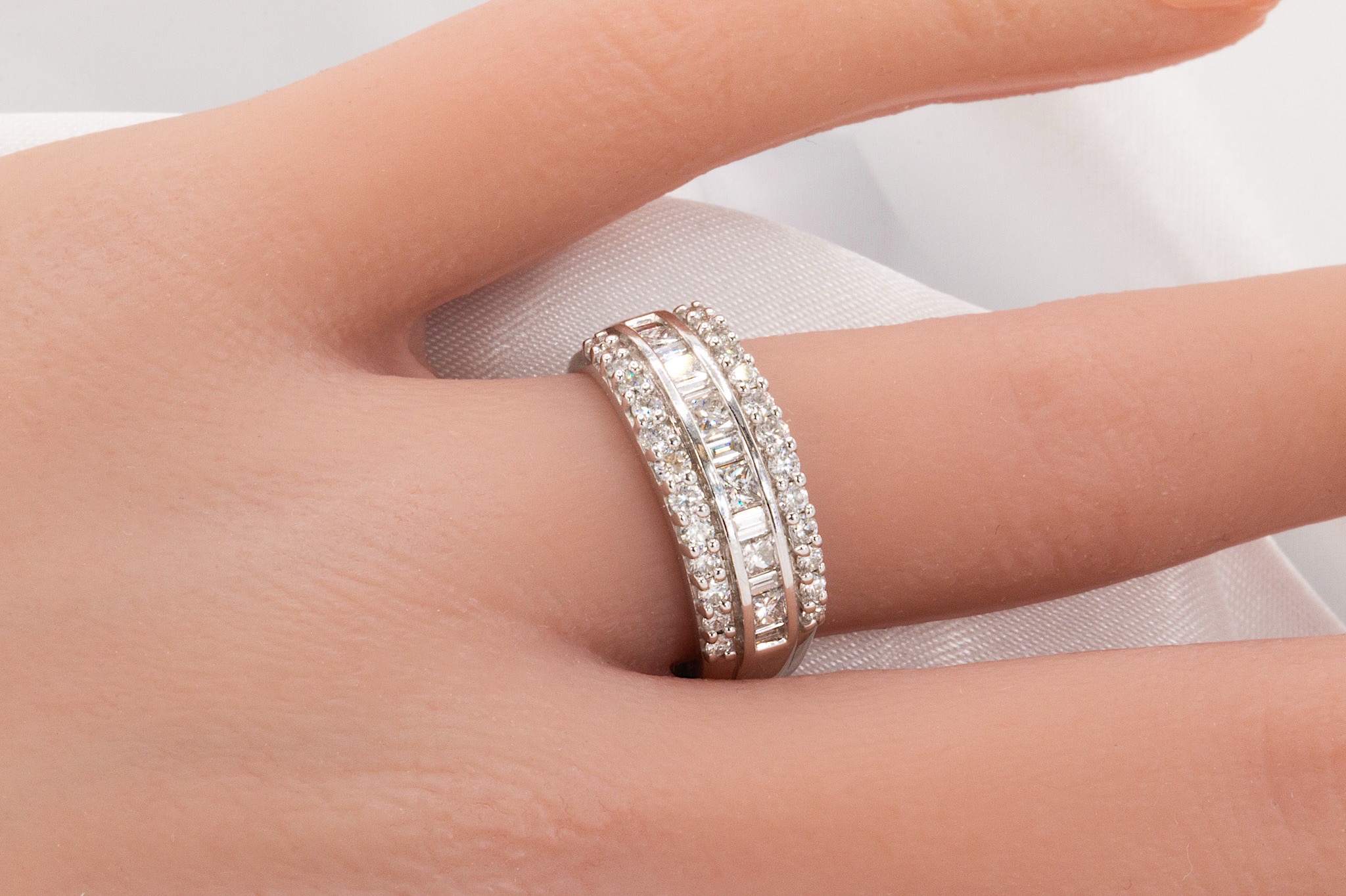 Close-up of a hand wearing two diamond-studded rings on the ring finger, with a light background.