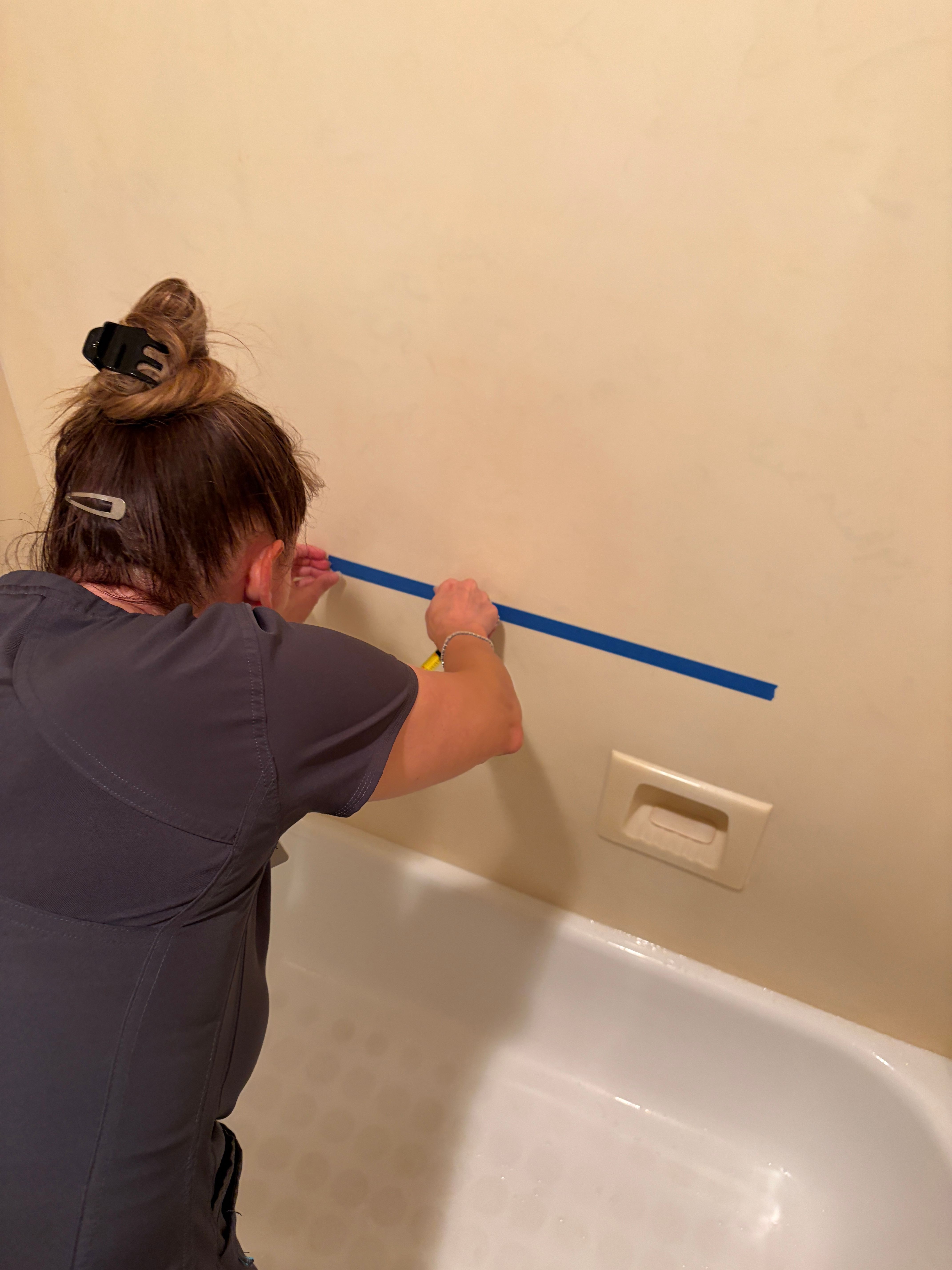 Person holding a blue stick in a bathroom, with a shower and wall switch visible.