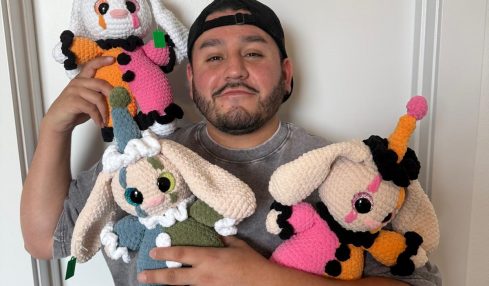 Person holding three colorful knitted animal toys, standing against a plain white wall.