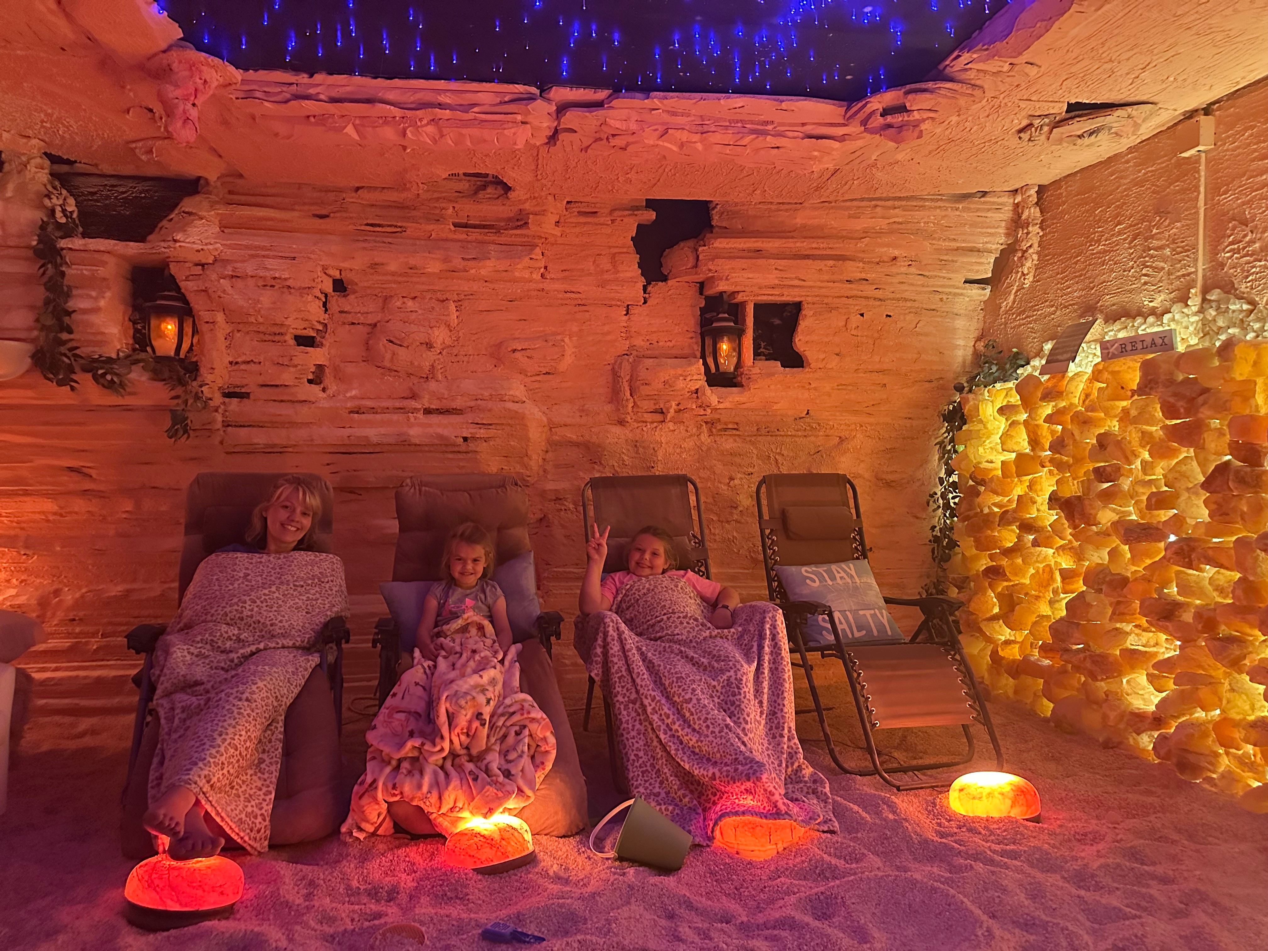 Three lounge chairs covered with blankets are in a cozy room with warm lighting and a decorative wall of yellow flowers.