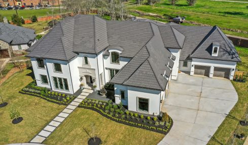 Large modern house with multiple roof sections, front walkway, and attached garage, surrounded by a well-maintained lawn and trees.