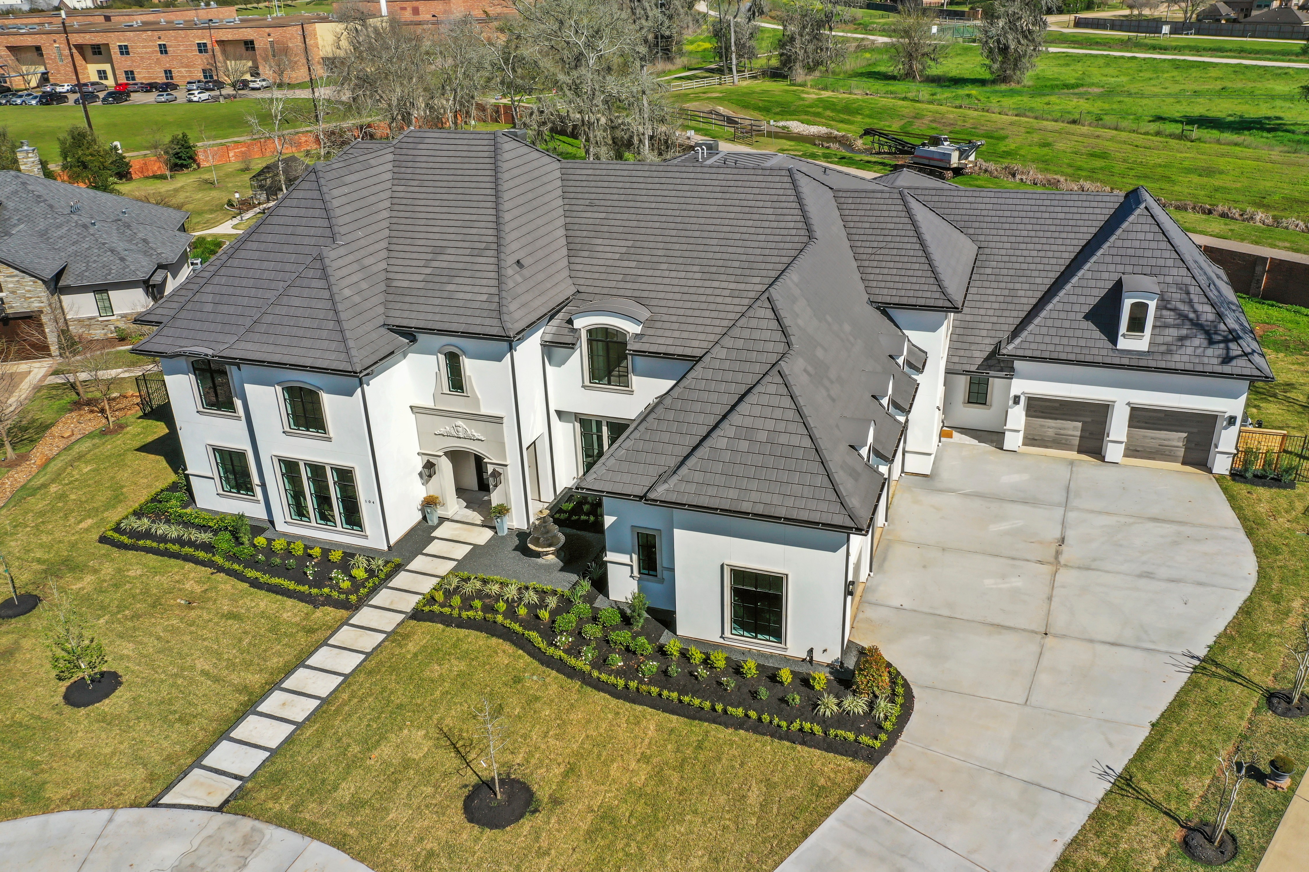 Large modern house with multiple roof sections, front walkway, and attached garage, surrounded by a well-maintained lawn and trees.