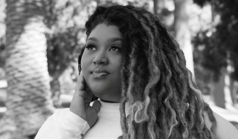 Young woman with long, curly hair outdoors, smiling, surrounded by trees, in black and white.